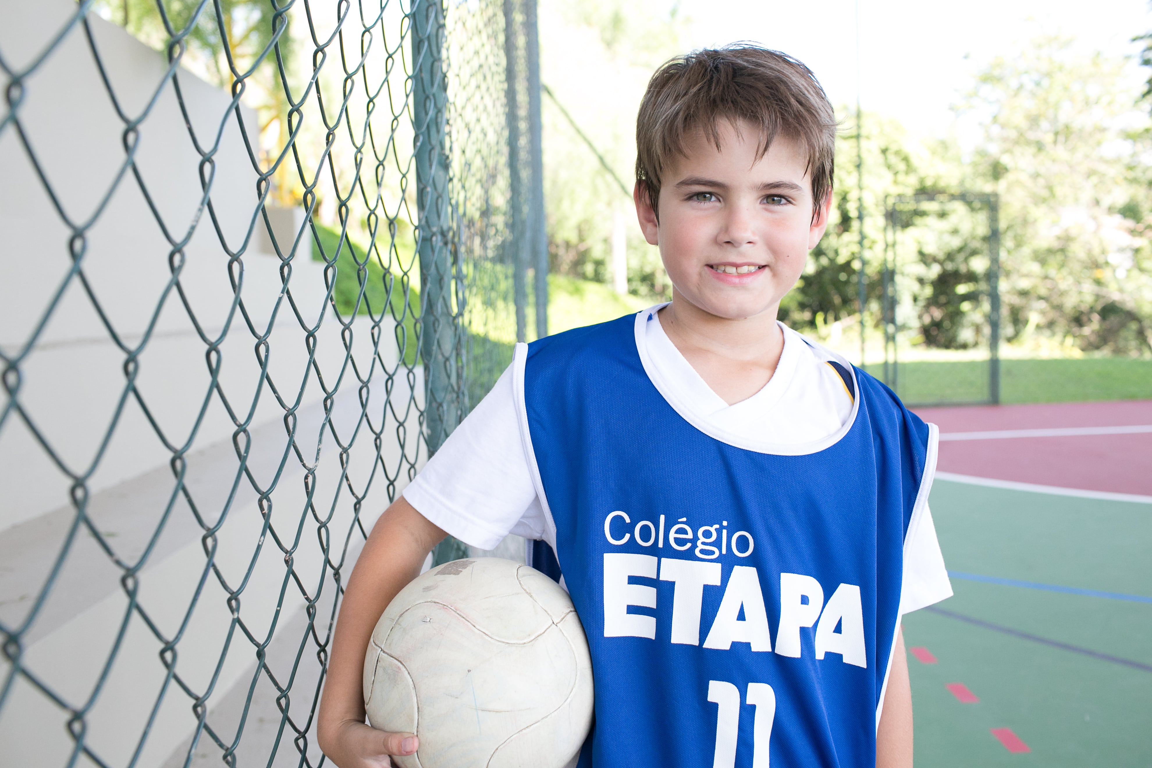 Criança com uniforme do Colégio Etapa segurando uma bola